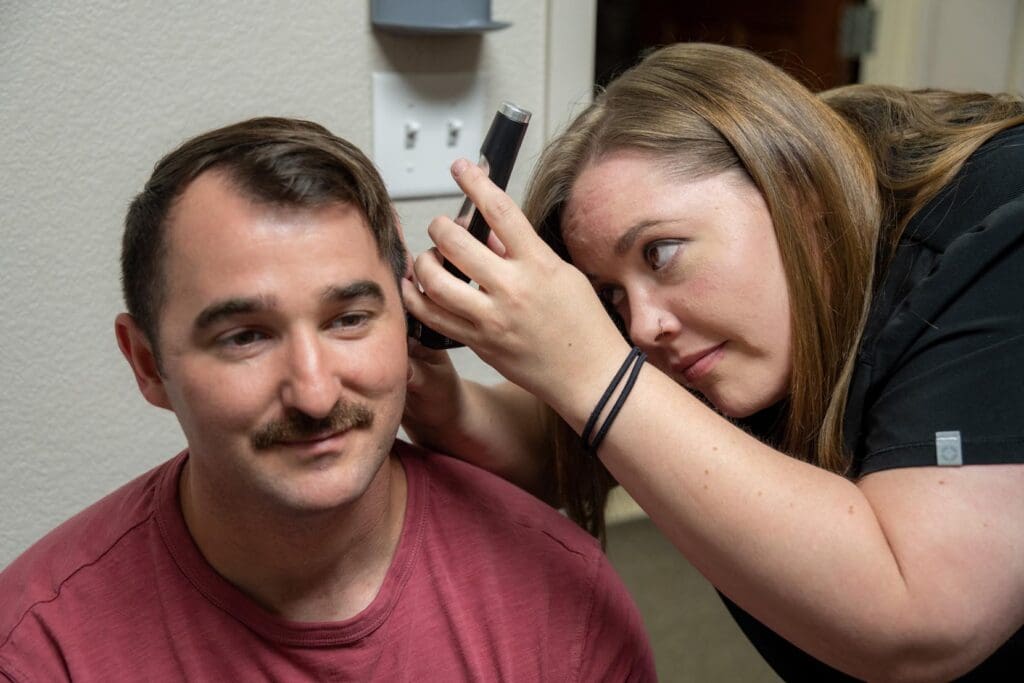 Man in a red shirt checked by a woman with otoscope