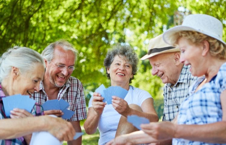 Group of happy seniors sitting outdoors and playing cards together on a sunny day.