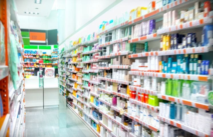 Aisle in a brightly lit pharmacy with shelves stocked with various over-the-counter medications and health products.